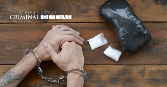 hands at table with handcuffs and drugs