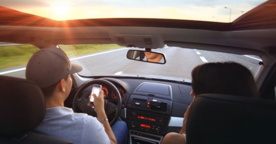 man and woman driving in car, man is texting while driving