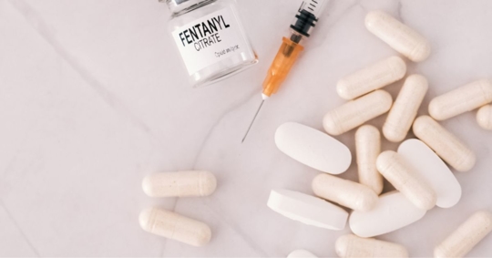 fentanyl, a needle, and pills laying on a white surface